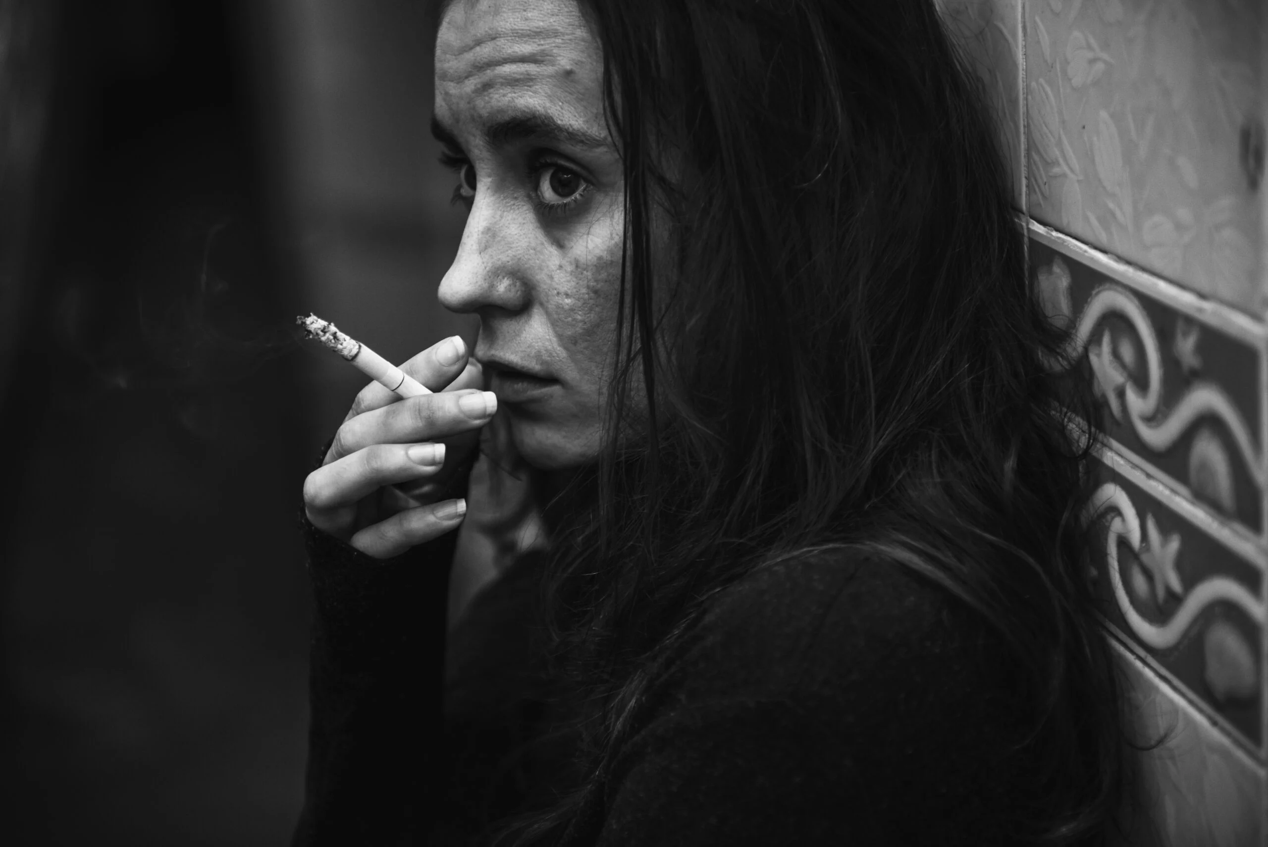 Retrato en blanco y negro de una mujer fumando con mirada perdida y expresión de angustia, representando la soledad y el impacto emocional de la drogodependencia.